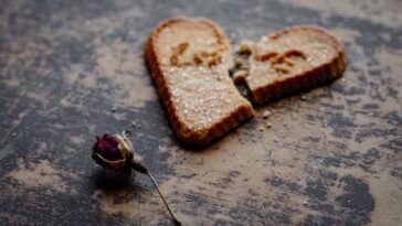 dry rose flower next to broken heart shaped cookie