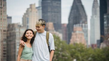 delighted young ethnic couple cuddling while standing against scenic cityscape with modern skyscrapers