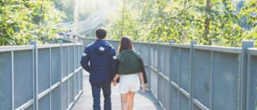 man and woman holdings hands while walking on bridge