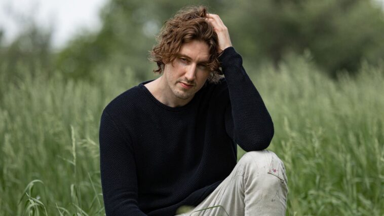 Dean Lewis's picture sitting and surrounded with green grasses